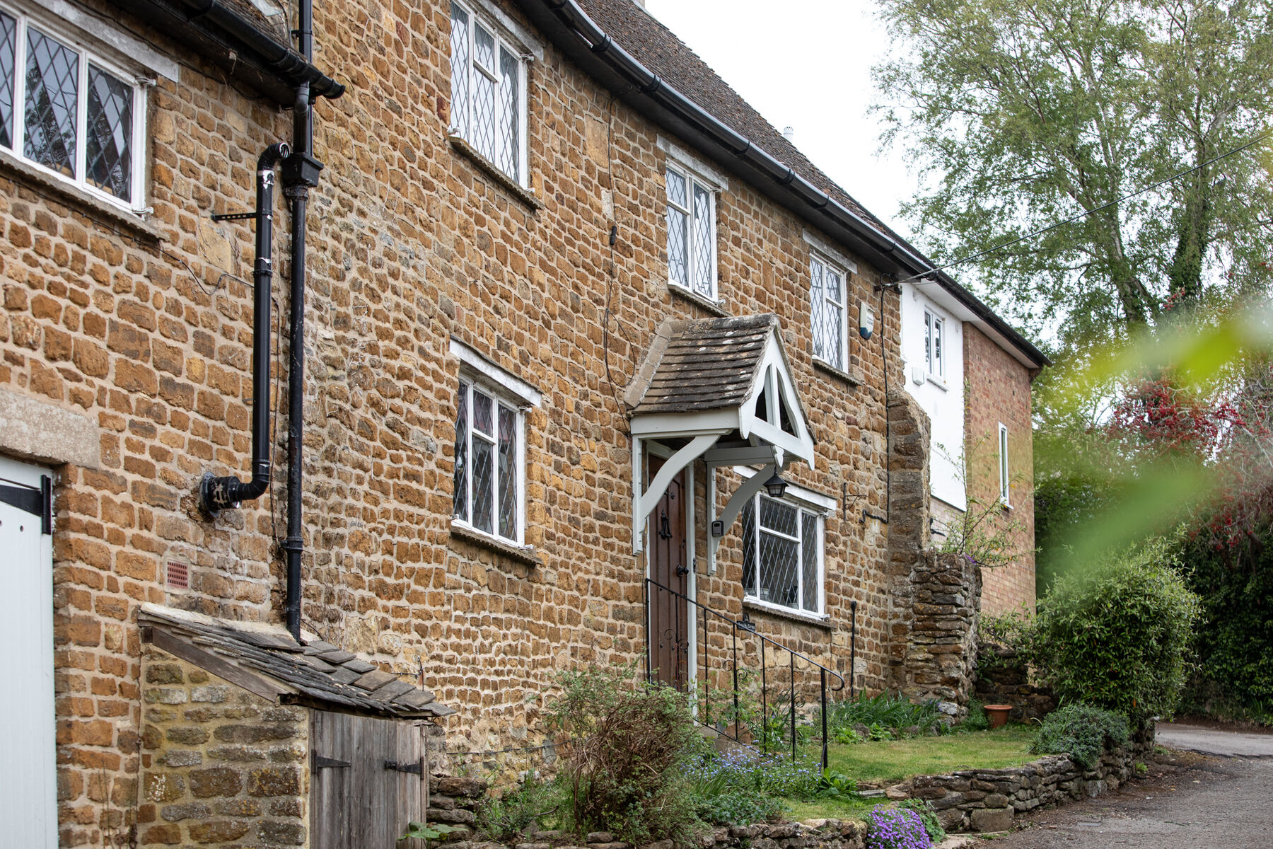 Bridge Hill Cottage, a honey-coloured ironstone cottage in Hook Norton, with its white gabled porch and front door