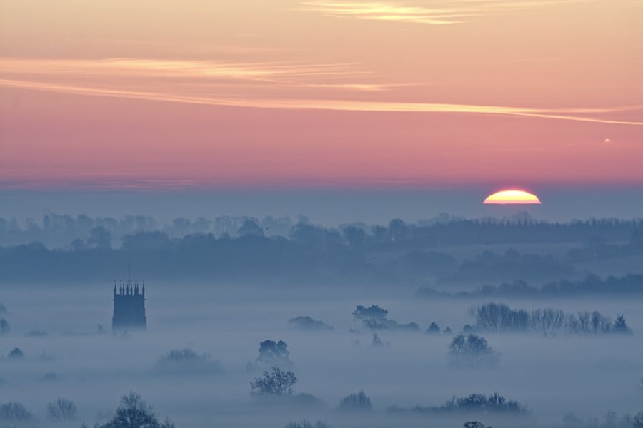 Hook Norton village at sunrise, the church tower rising through morning mist